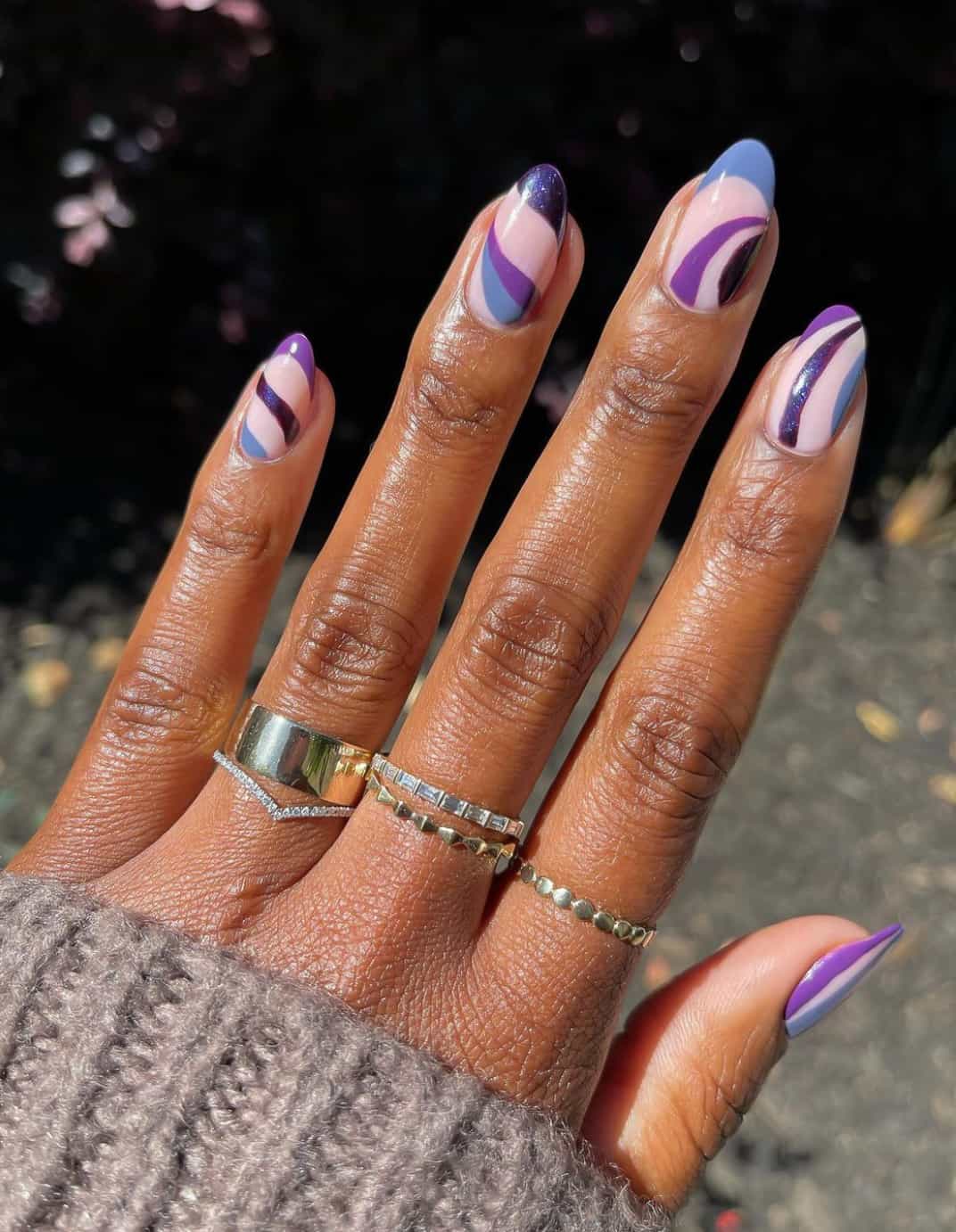 A hand with medium length round nails with a nude pink base and swirls in multiple shades of purple
