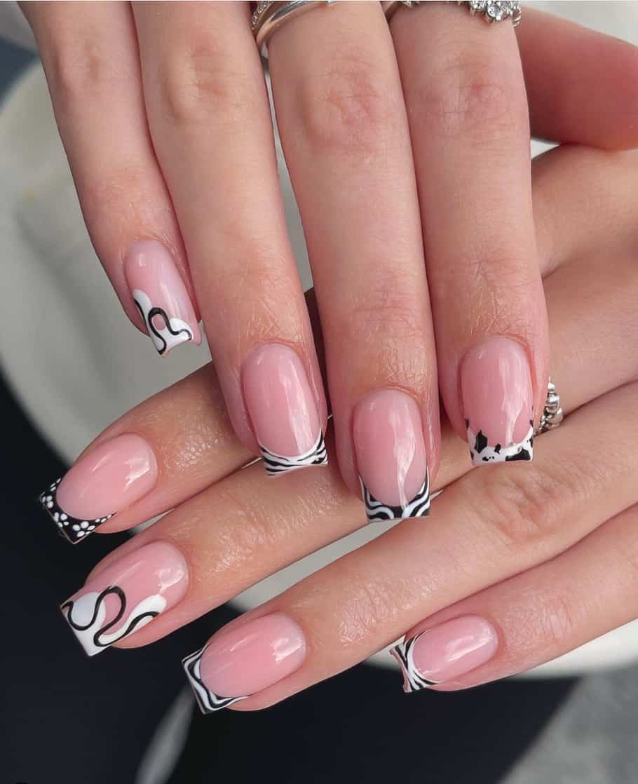 A hand with pink nude square nails featuring black and white French tips with swirls, line patterns, and splatter designs