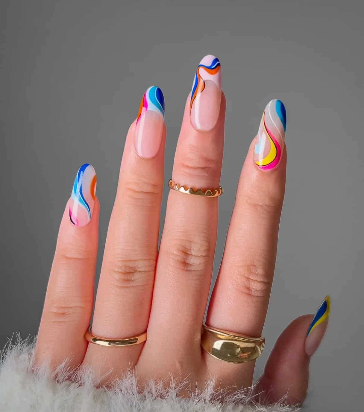 A hand with long round nails that have a glossy nude base with rainbow swirls and French tips