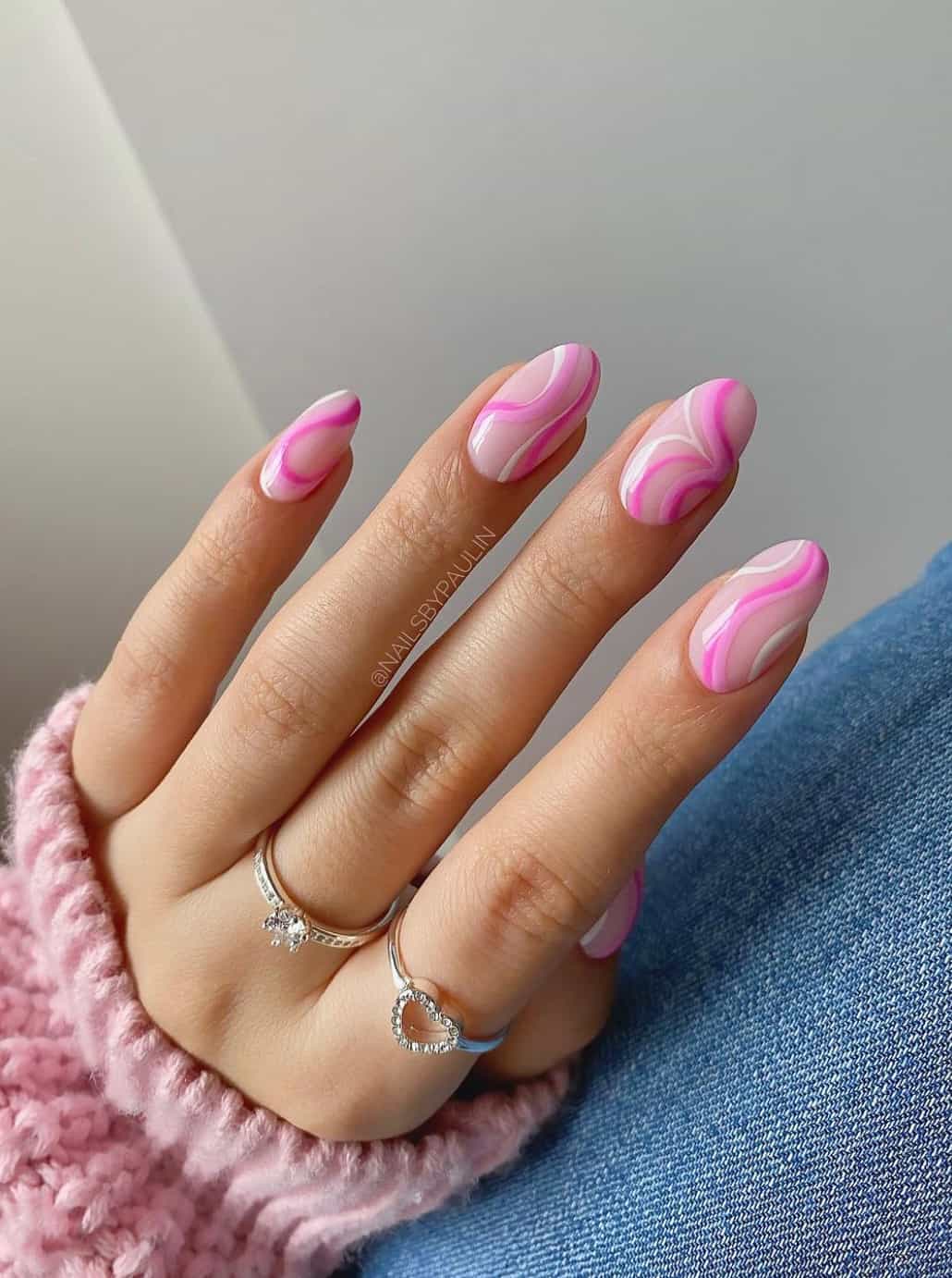 A hand with light pink round nails featuring dark pink, medium pink, and white swirls