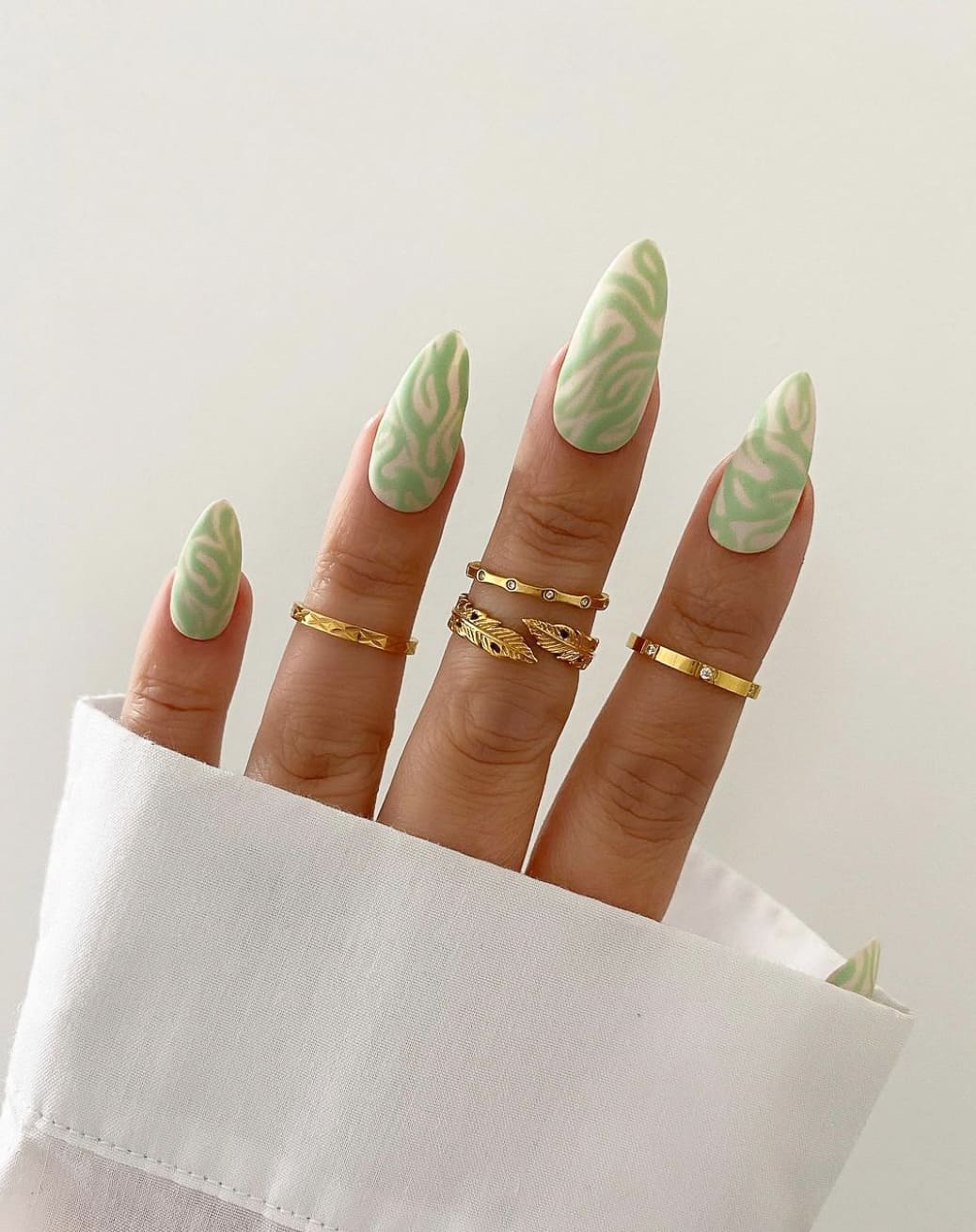 A hand with matte white stiletto nails with light green swirls