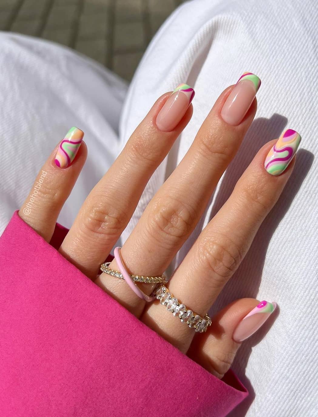 A hand with nude square nails with magenta, orange, and lime green swirl accents and French tips