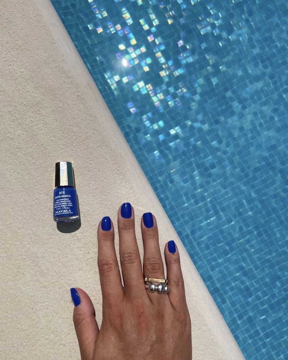 A hand by the pool with short solid royal blue nails