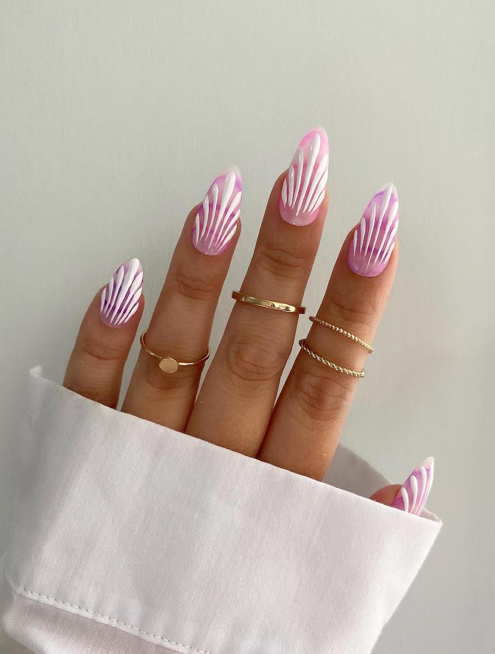 A hand with long almond nails painted to look like seashells with light and dark pink polish and white accent lines