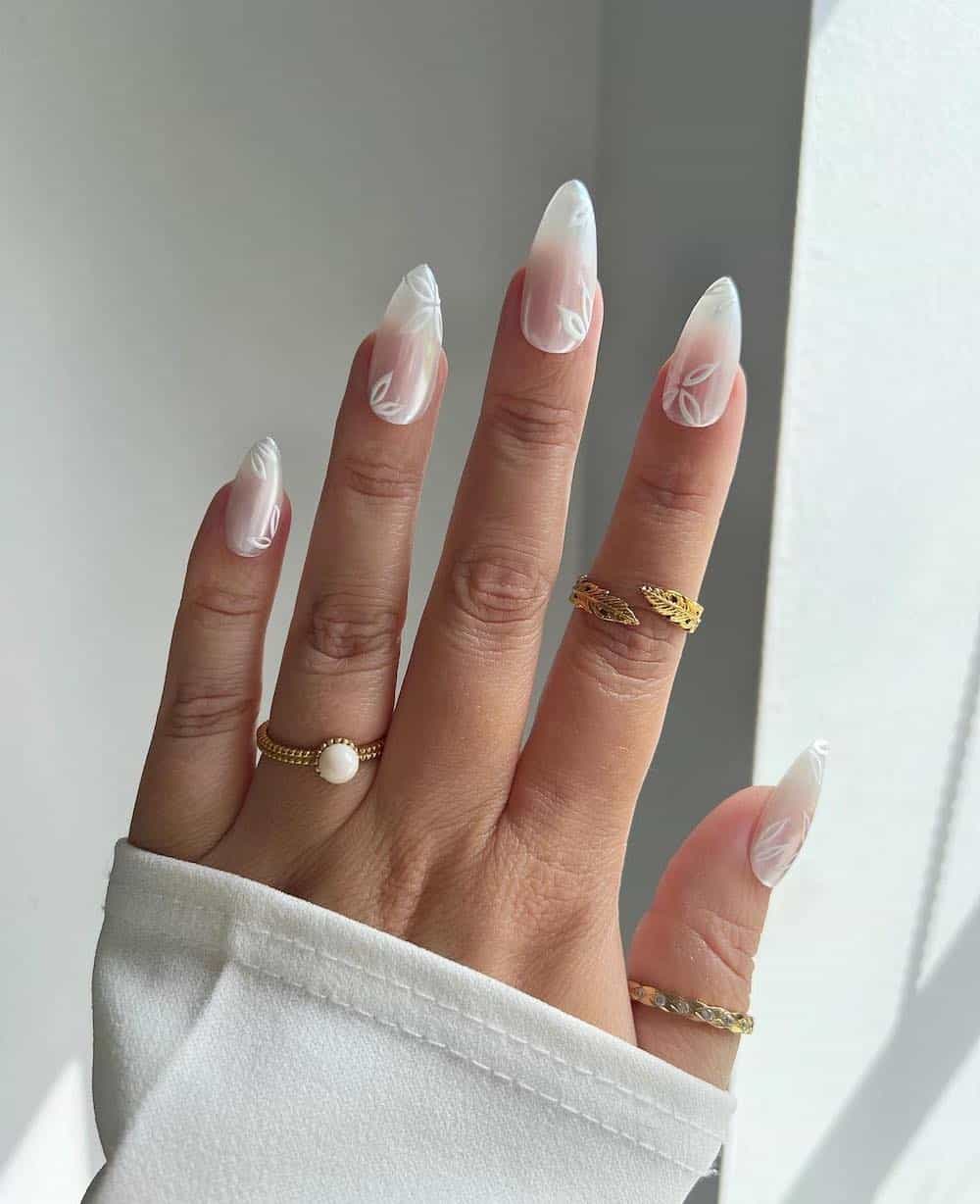 A hand with long stiletto nails featuring the glazed donut manicure with white flower accents