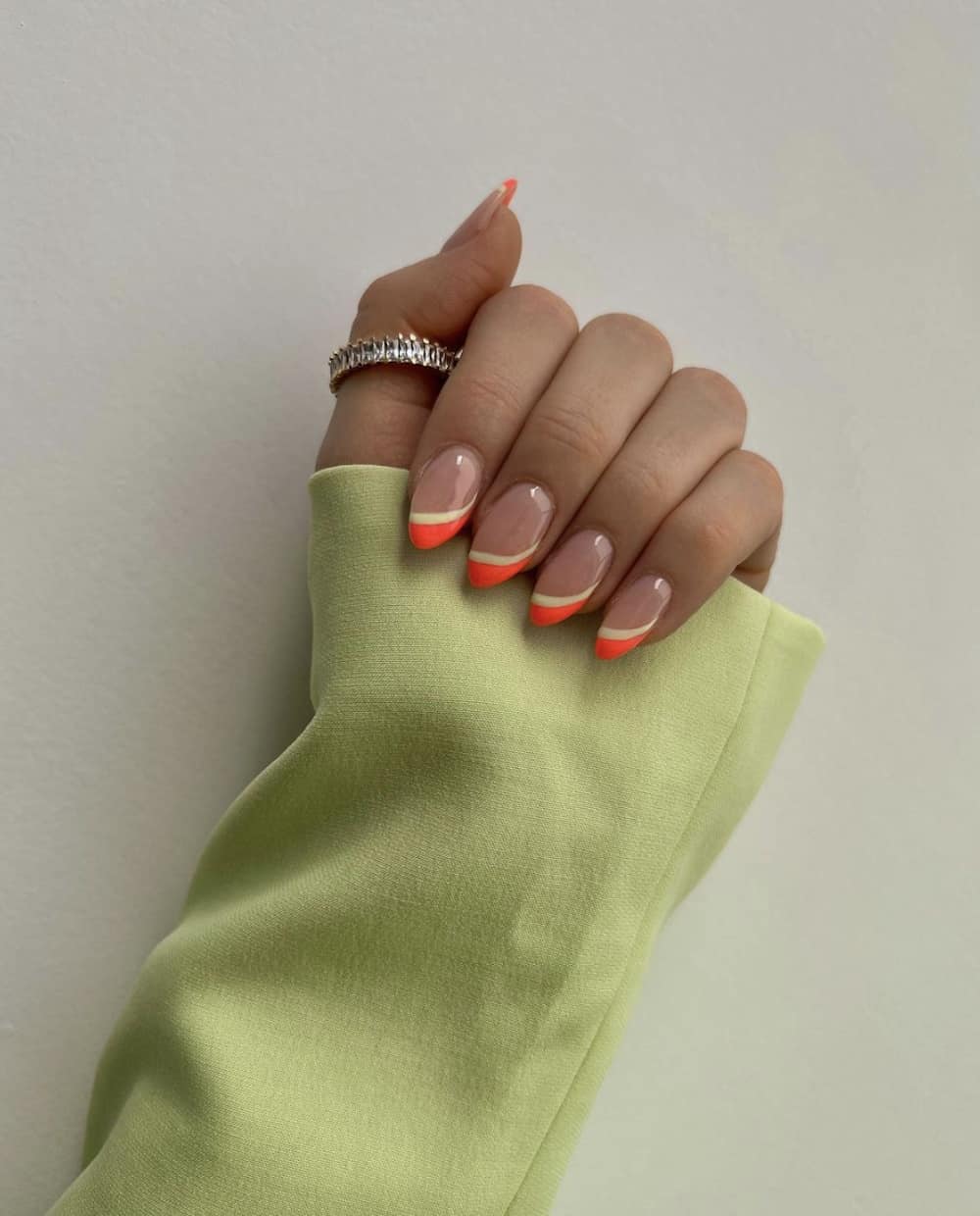 A hand with glossy nude almond nails and asymmetrical neon orange and yellow French tips