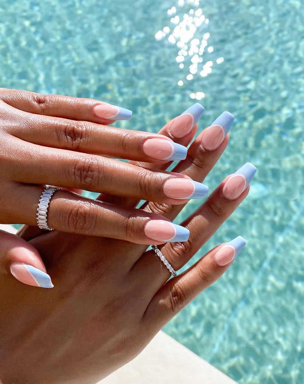 A hand with long coffin nails with line blue French tips and white lines underneath