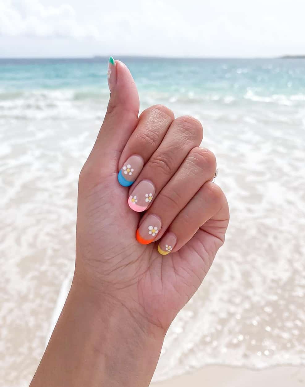 A hand with medium-length round nails with gradient French tips and white flower accents