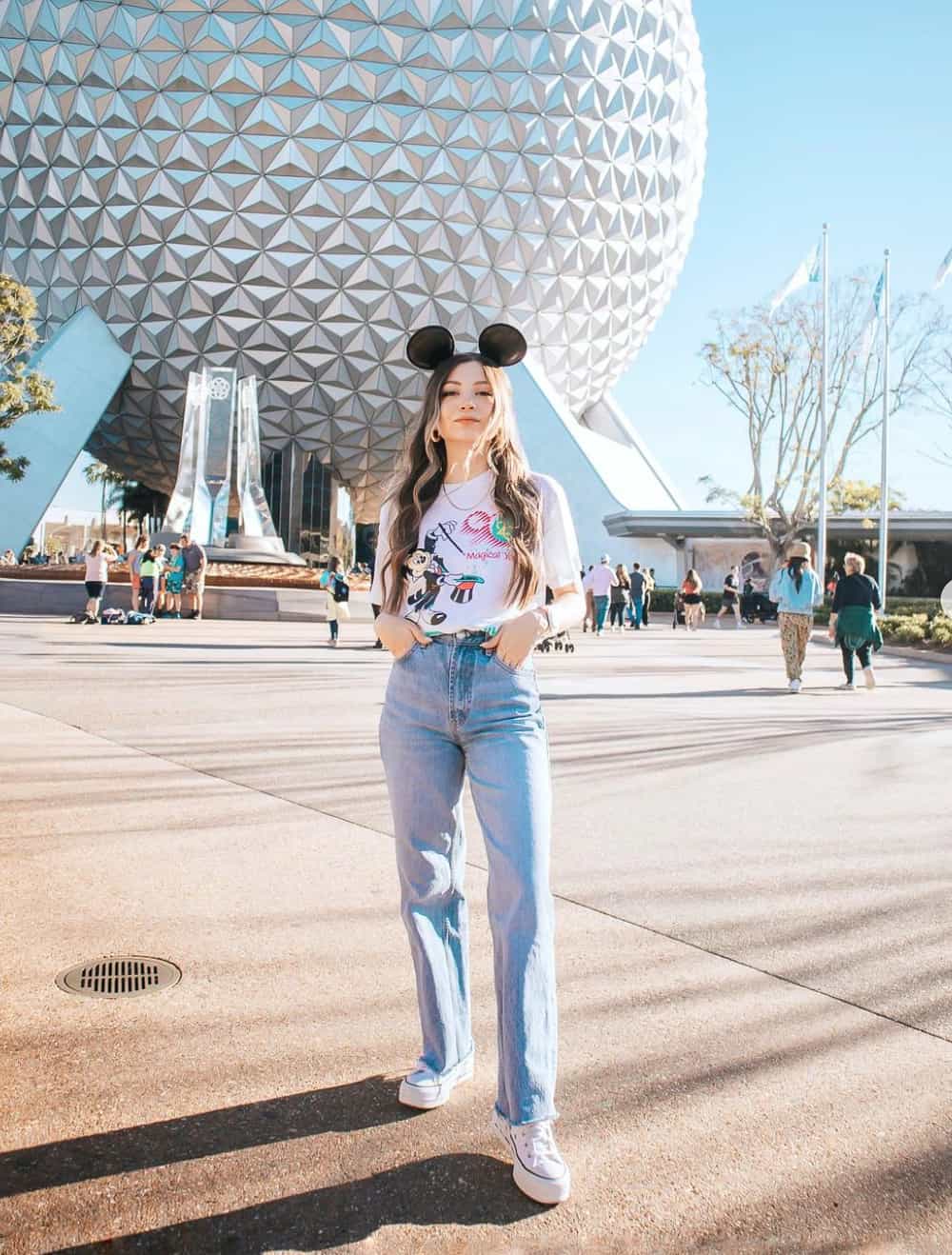 Woman at Disney World wearing an outfit with blue jeans and a Mickey t-shirt with sneakers and Mickey Mouse ears