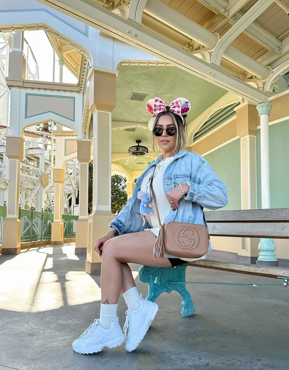 Woman wearing a denim jacket over an oversized t-shirt with biker shorts and sneakers and Minnie ears at Disney World