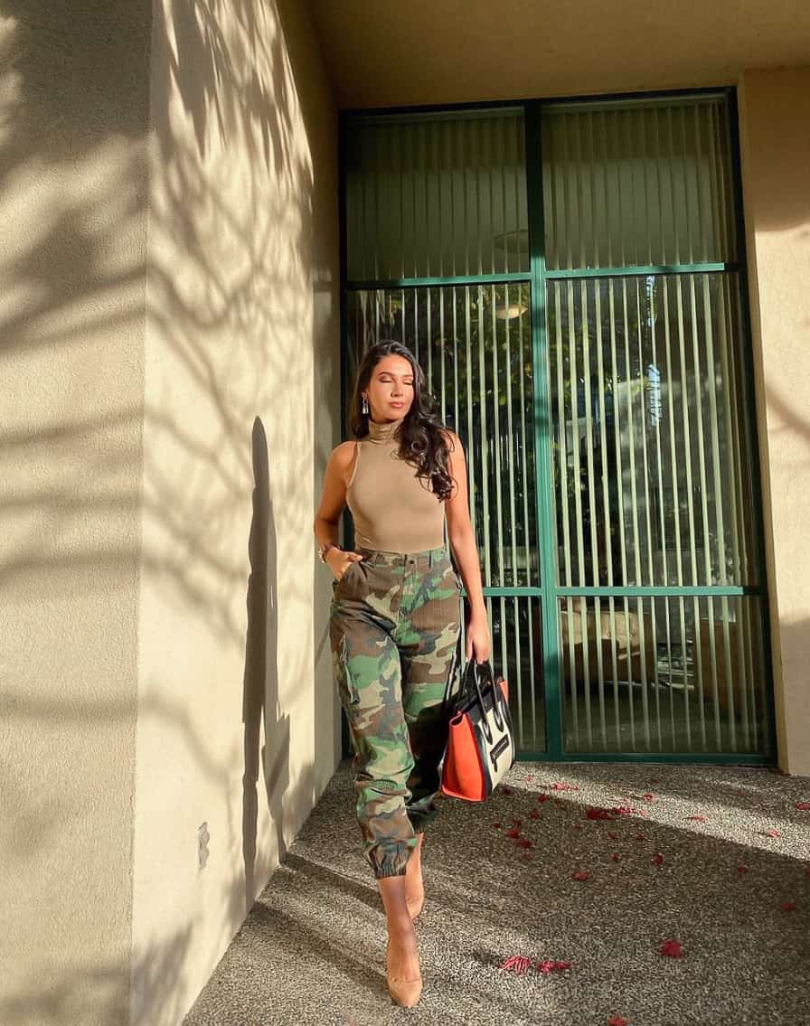 A woman wearing camo pants with a beige turtleneck tank top and nude colored pumps