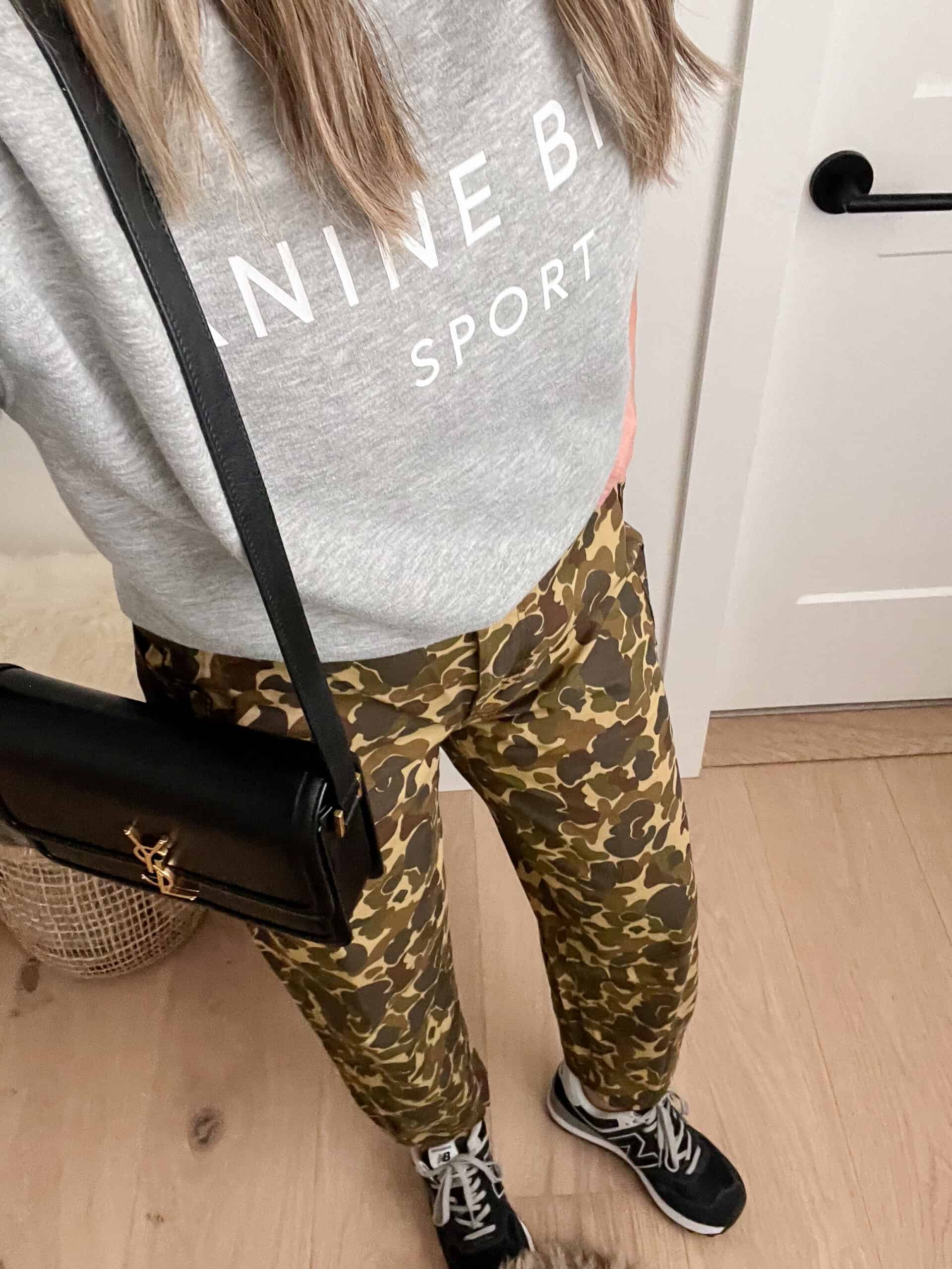 An overhead shot of a woman wearing camo pants with a grey sweatshirt and black trainers with a black crossbody bag