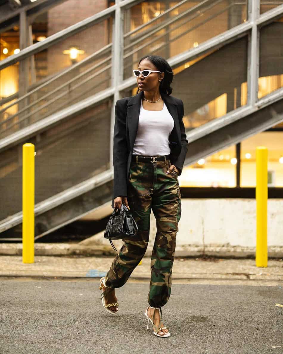 A woman wearing camo pants with a white tank top, a black blazer, and strappy heels