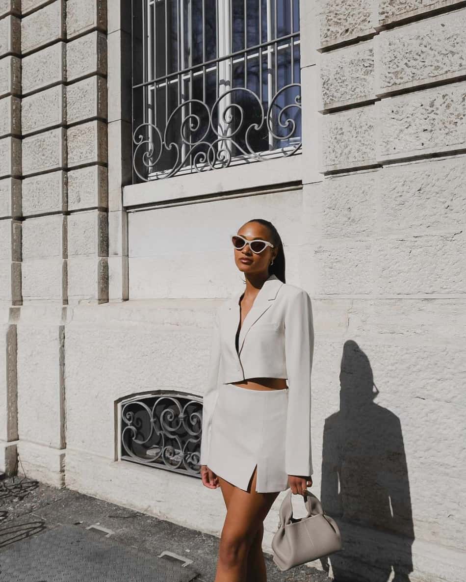 A woman wearing a white slitted mini skirt with a matching cropped blazer and a grey handbag