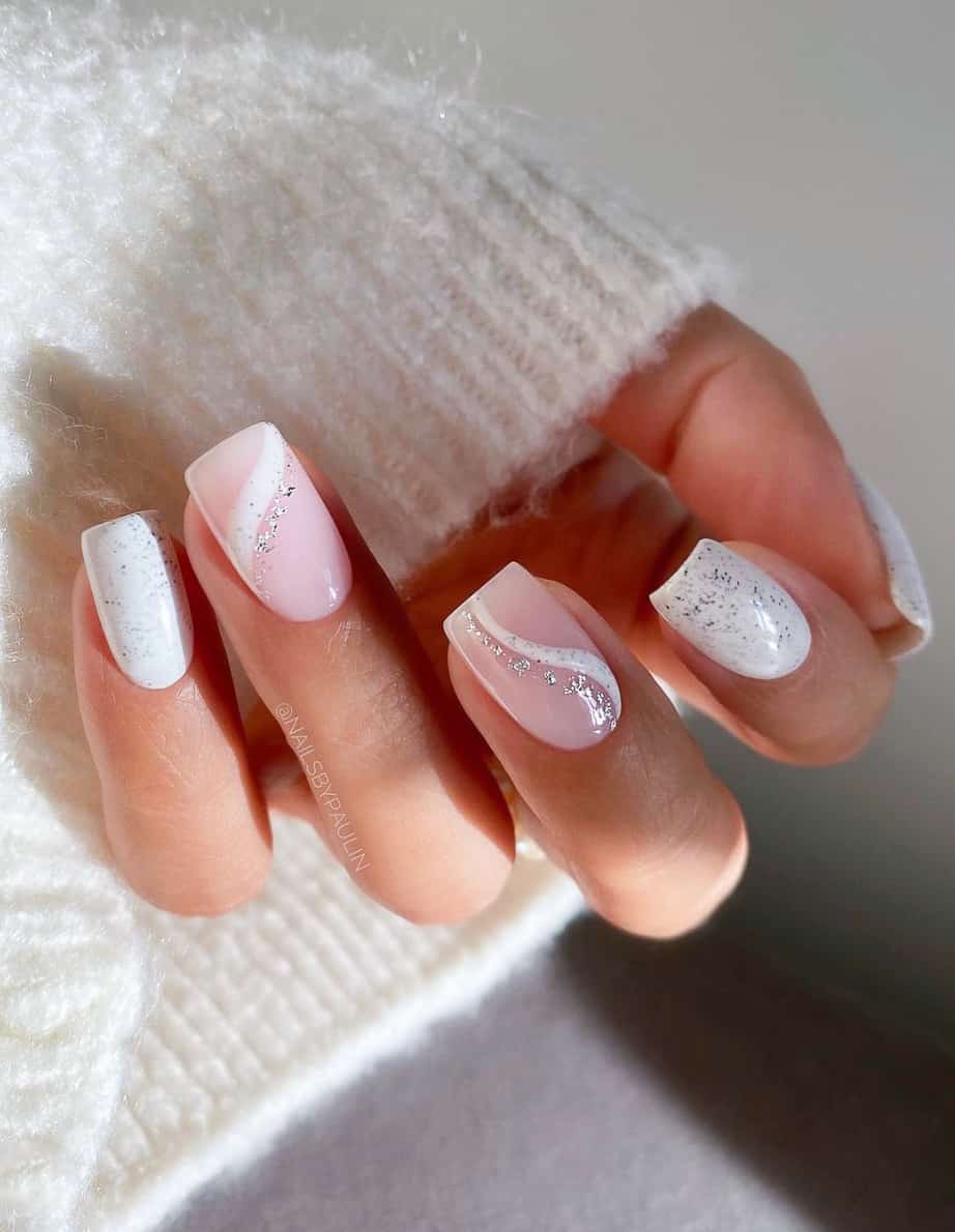 A hand with white square nails with two nude pink accent nails featuring white swirls with silver glitter