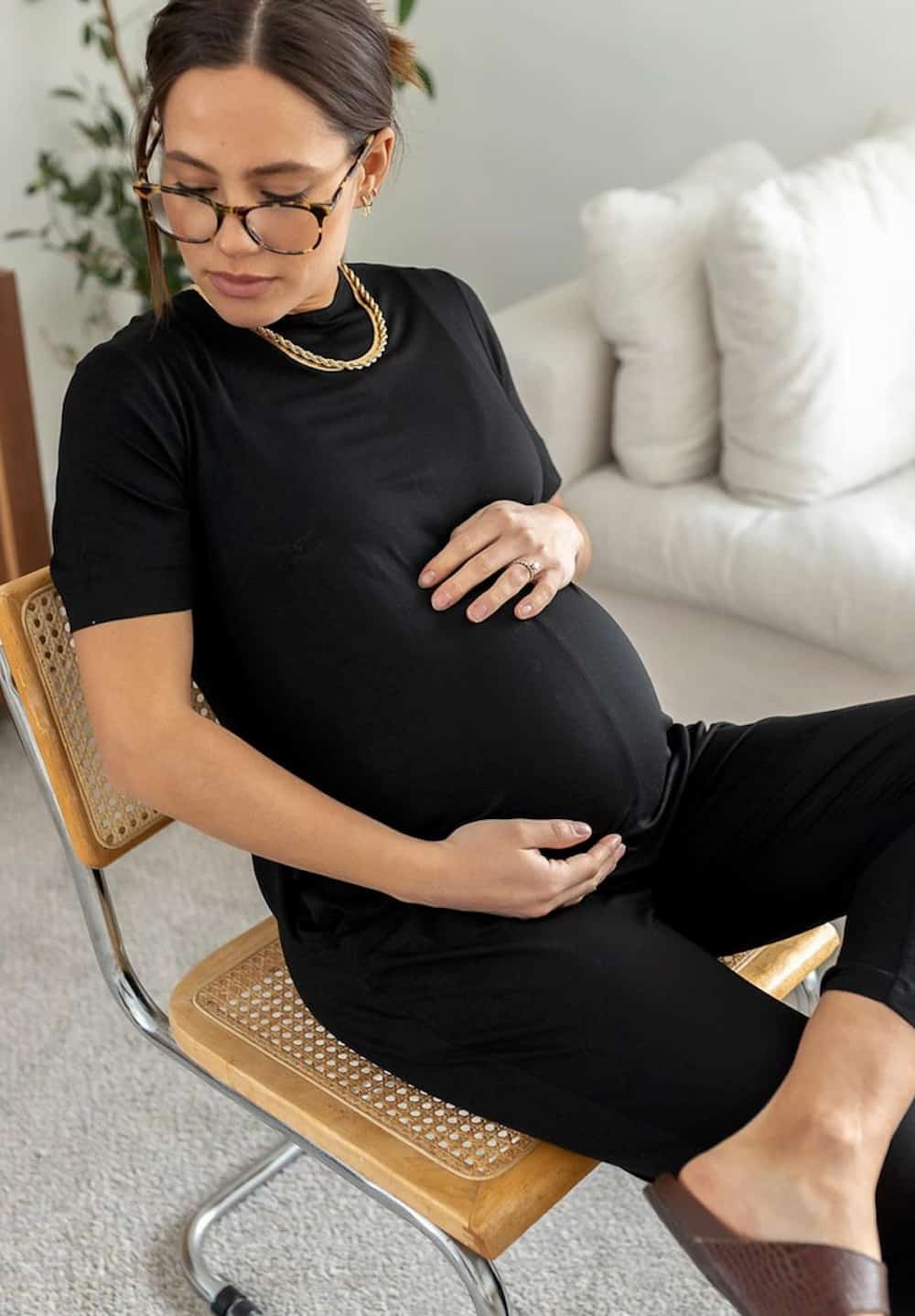 Pregnant woman sitting in a chair wearing a black short-sleeved jumpsuit romper
