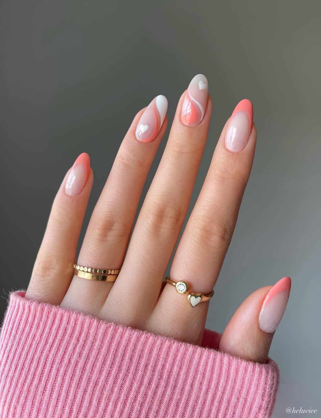 A hand with medium nude almond nails painted in coral peach French tips with white and coral peach wave accent nails with a heart detail