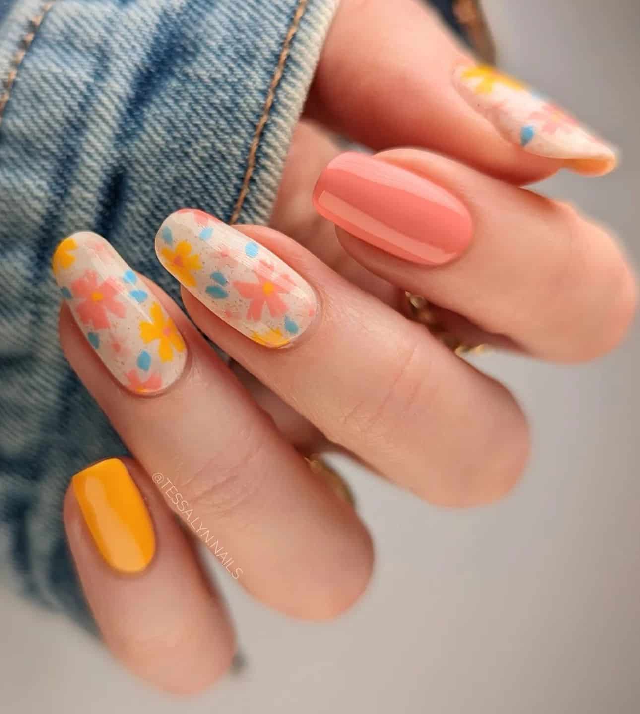 A hand with medium round nails painted with white polish with yellow and coral peach flowers, and two accent nails painted in solid colors