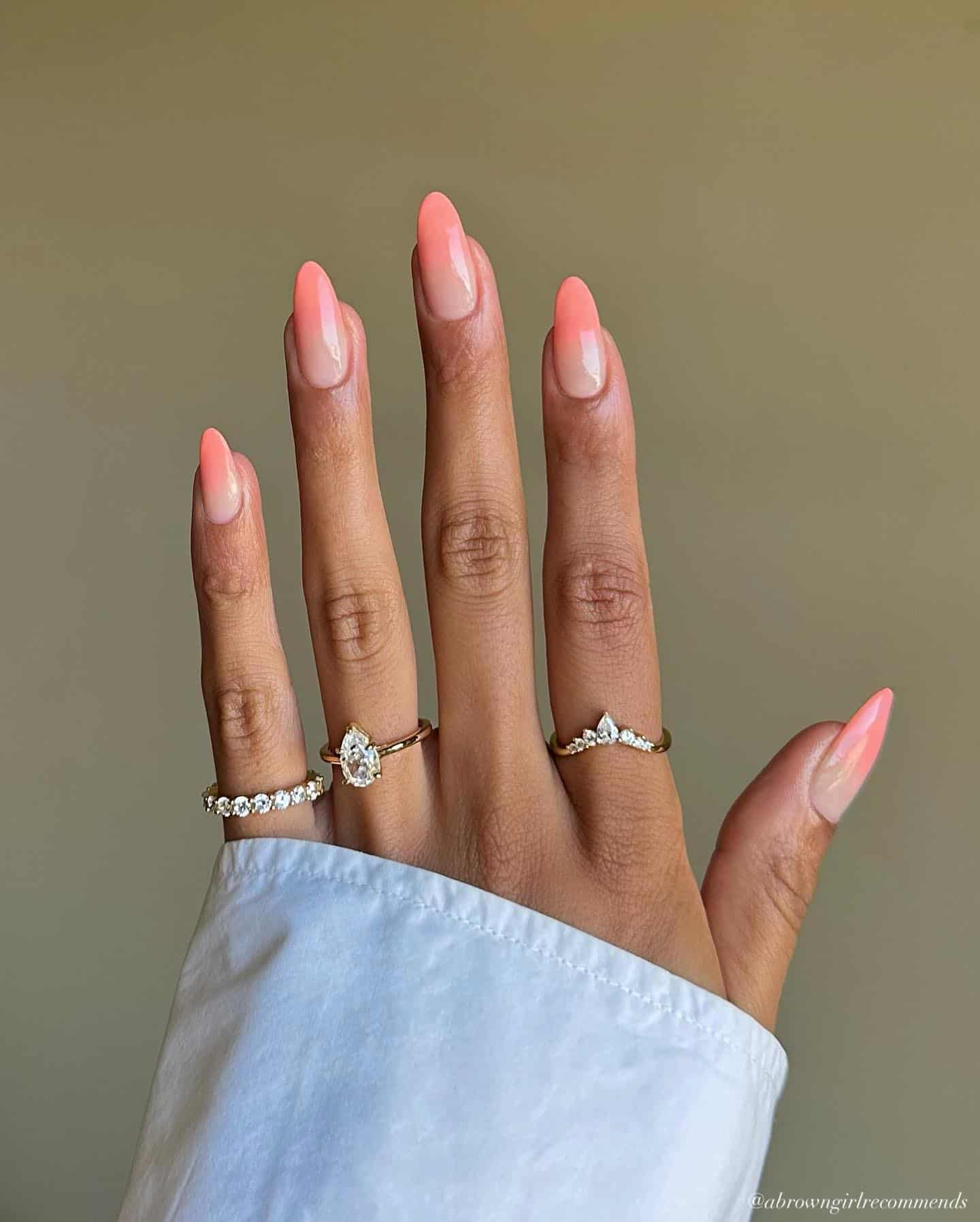 A hand with long round nails painted in a nude and coral peach ombre