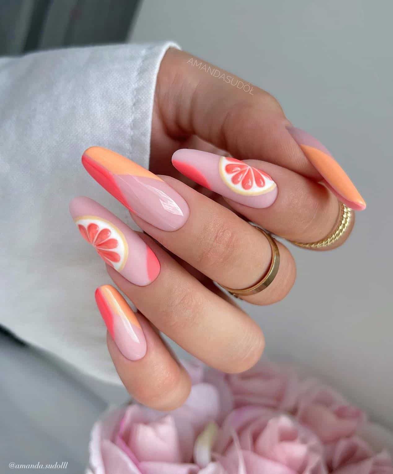 A hand with long almond nails painted a nude pink with peach and coral peach French tips and grapefruit nails art