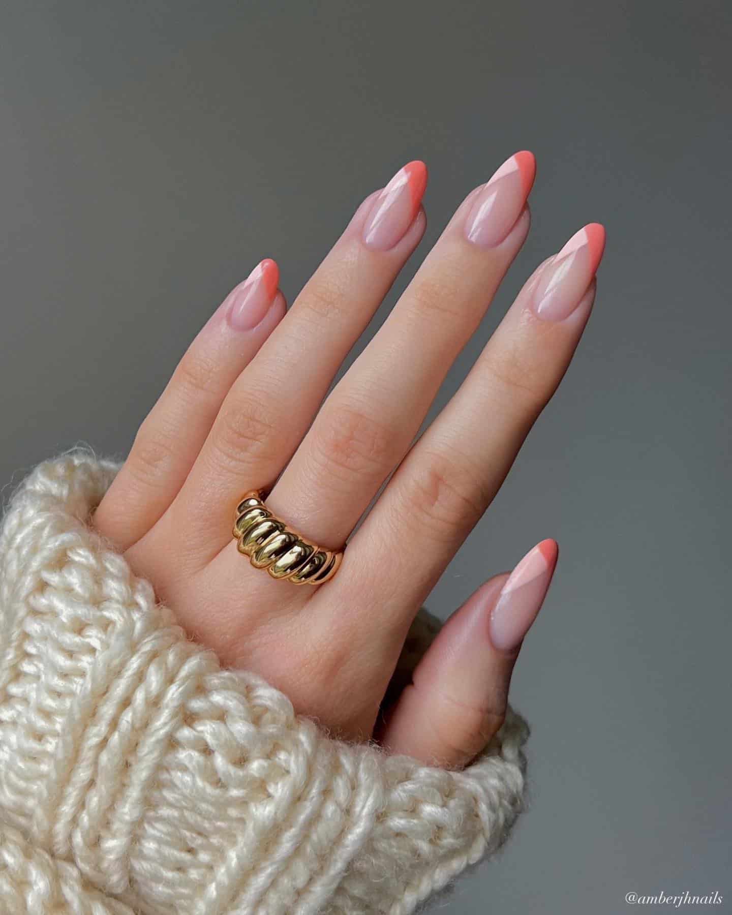A hand with medium almond nails painted with pink and coral peach French tips