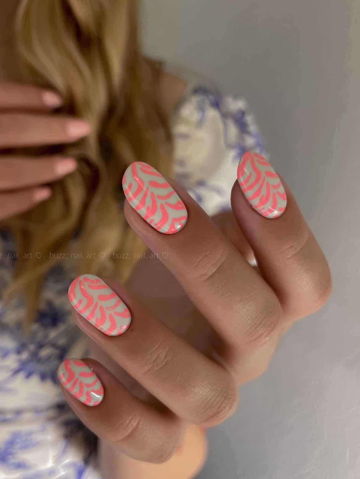 A hand with short round nails painted in a zebra print with coral peach and pastel green nail polish