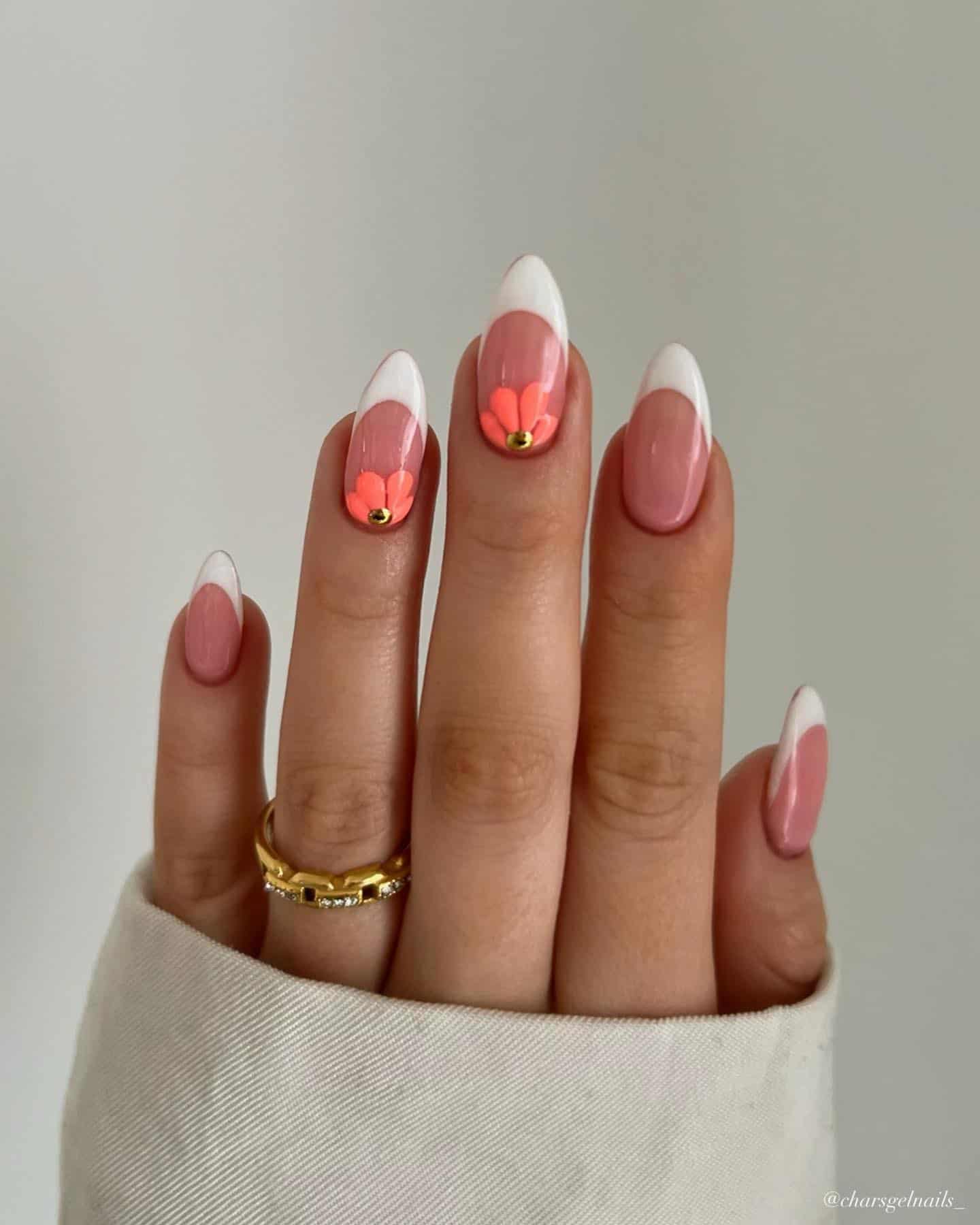 A hand with medium almond nails painted with white French tips and two coral peach accent flowers with gold gems
