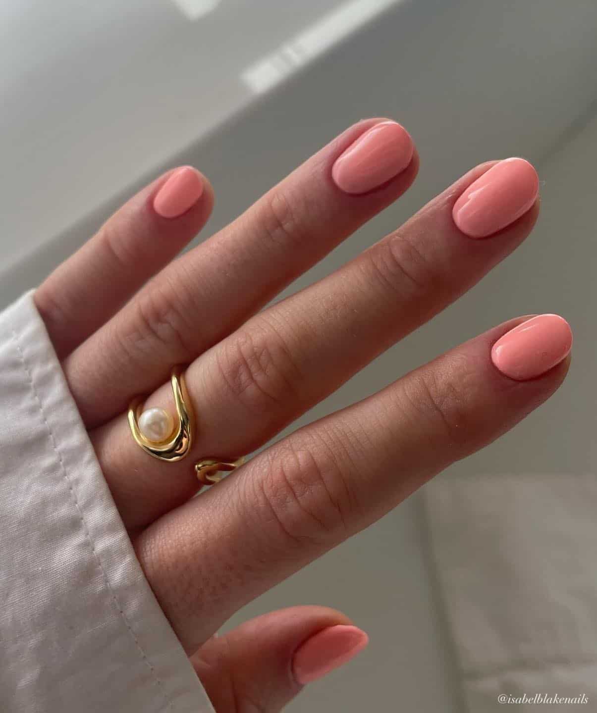 A hand with short round nails painted a soft coral peach color