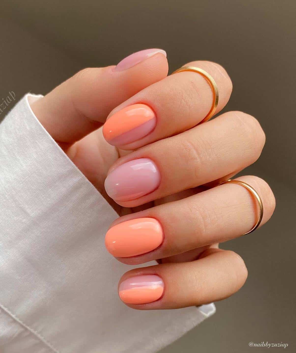 A hand with short round nude nails painted with a coral peach polish featuring solid colored nails and half painted nails