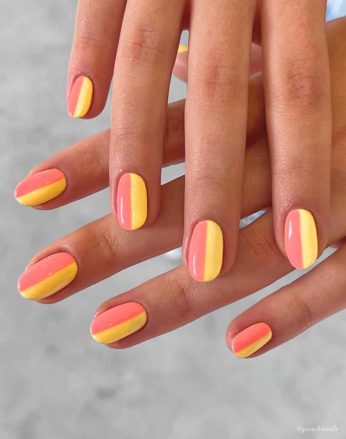 A hand with short round nails painted in a color block design with coral peach polish and yellow polish