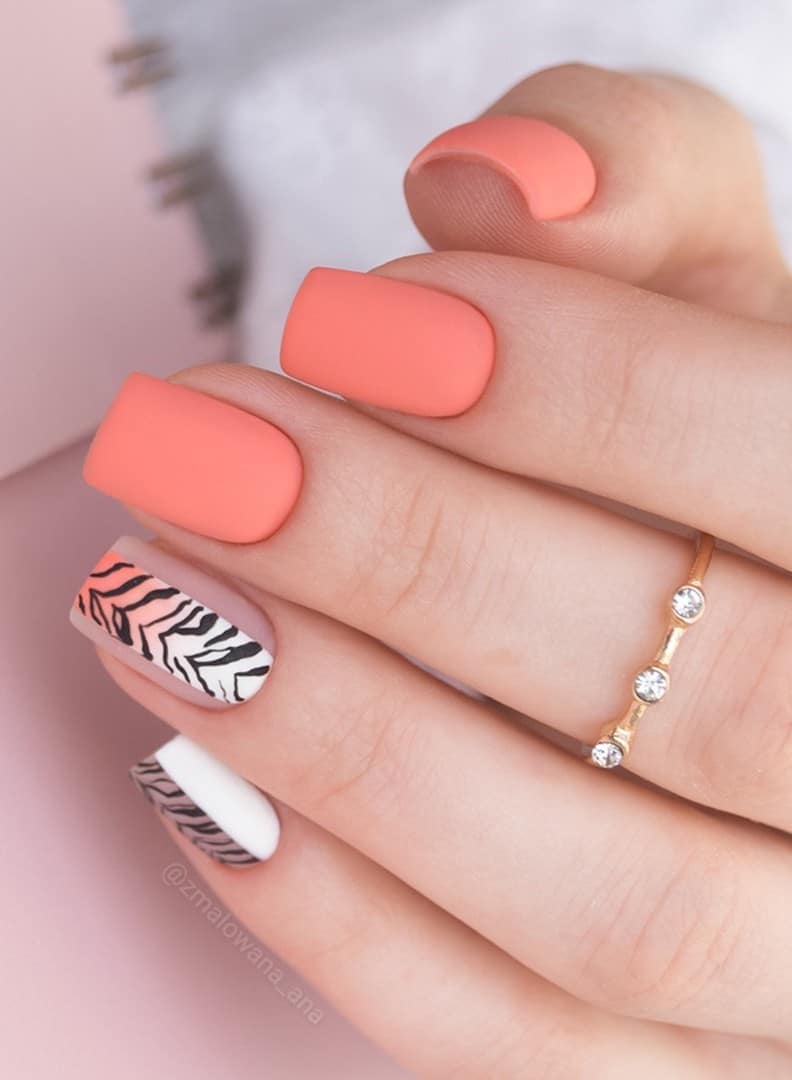 A hand with short square nails painted a nude coral peach color and two accent nails with white and black zebra stripes