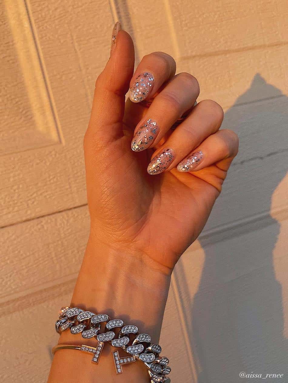 A hand with short almond nails covered in silver metallic flakes