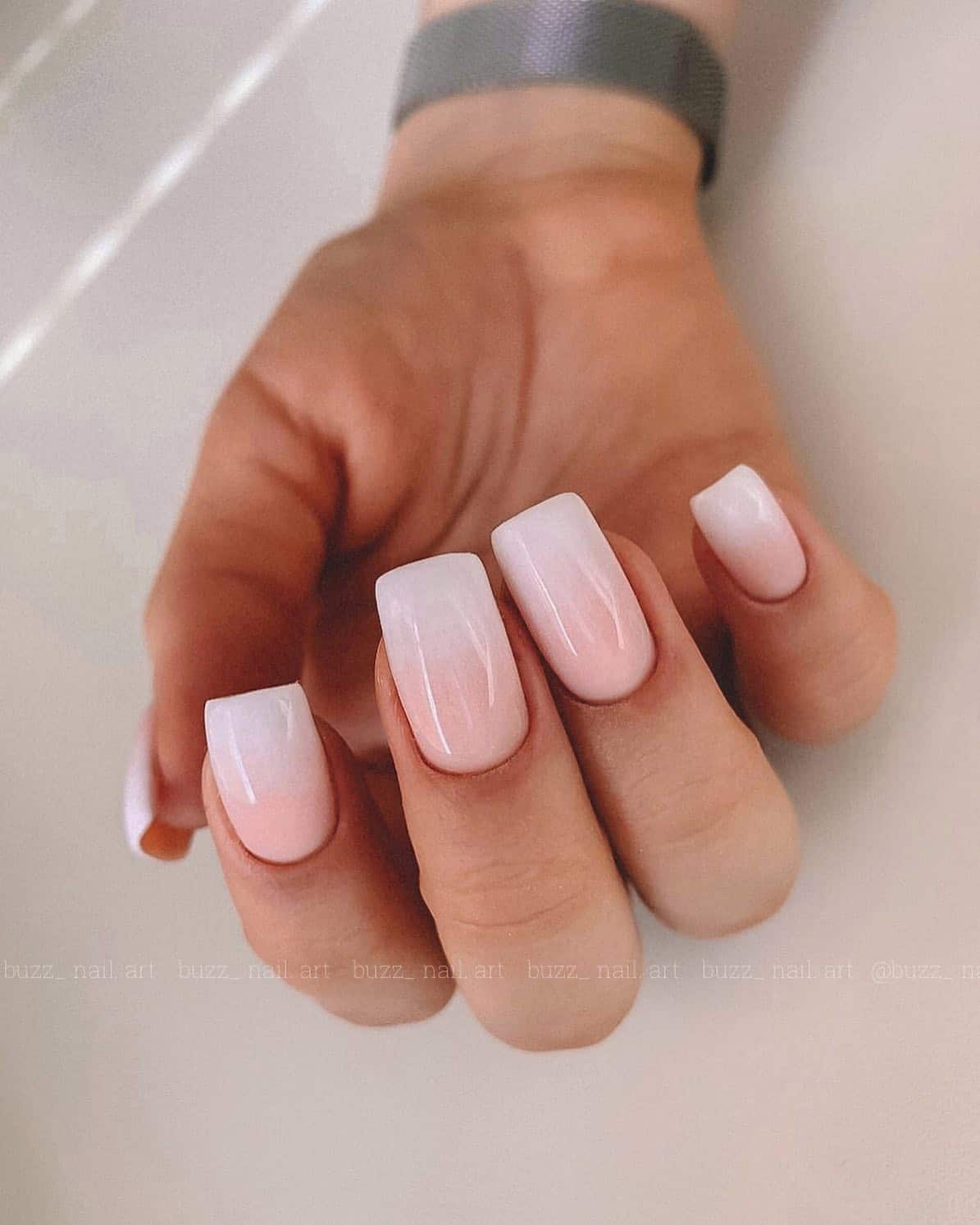 A hand with medium square nails painted a white and pink ombre