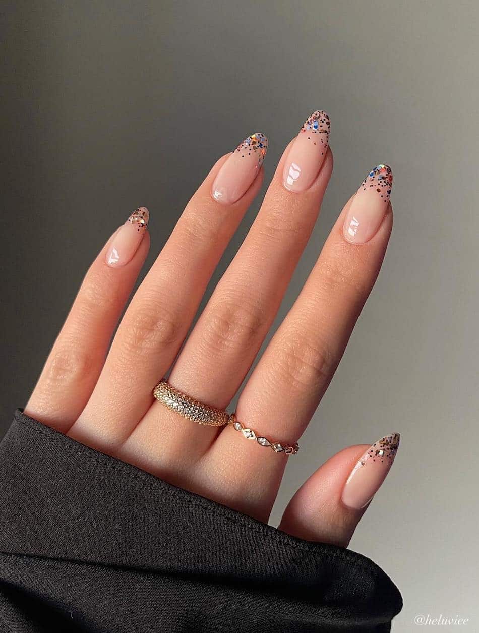 A hand with medium nude almond nails with rainbow glitter French tips