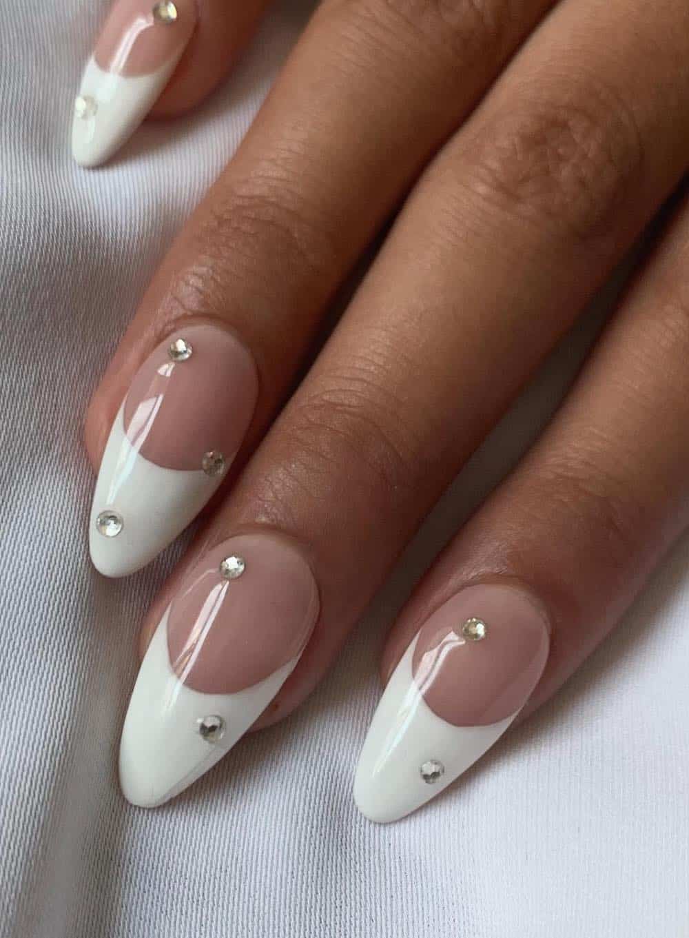 image of a hand with nude almond nails with white french tips and rhinestones