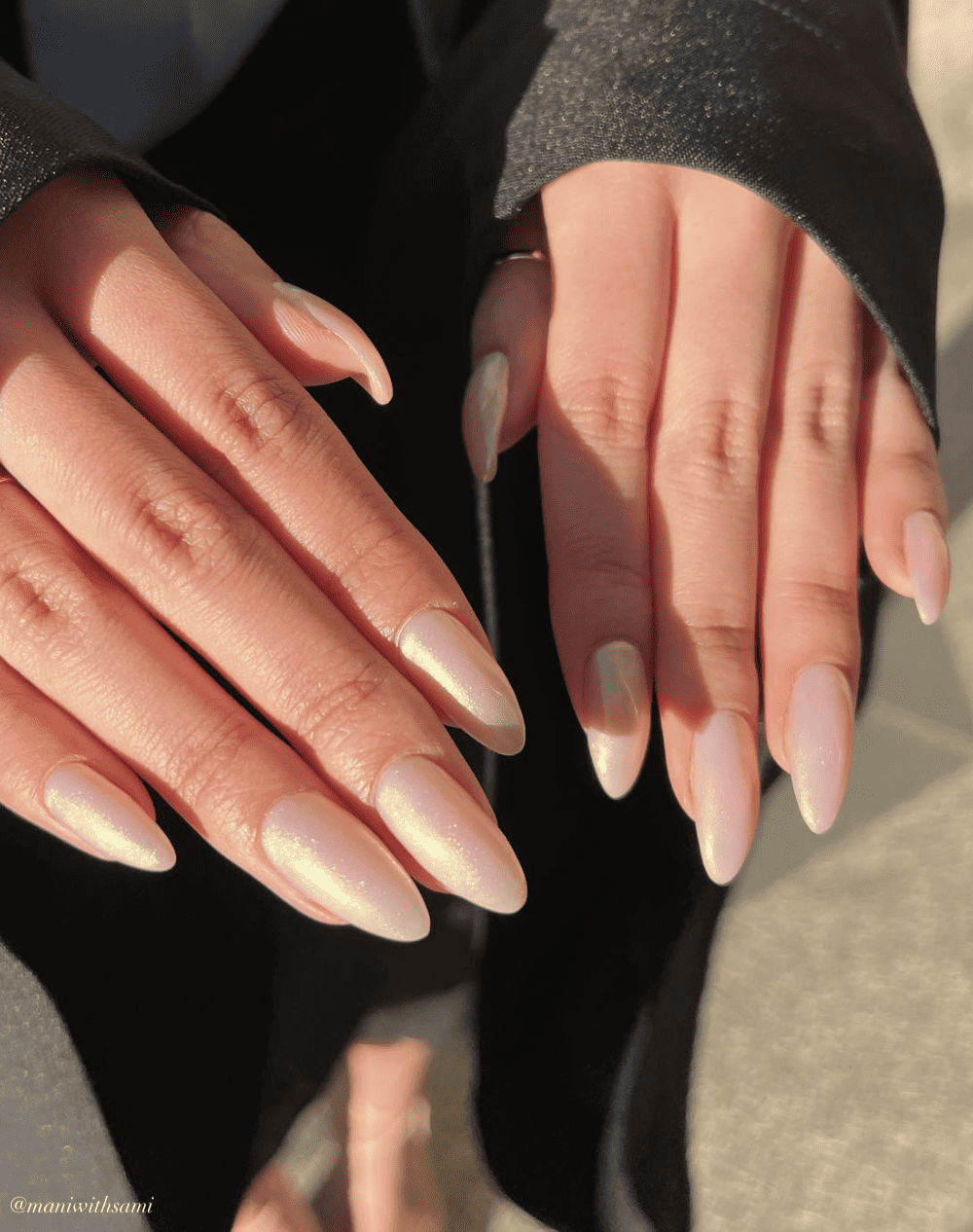 A woman's graduation nails featuring a nude pink polish on almond nails with a shimmering chrome finish