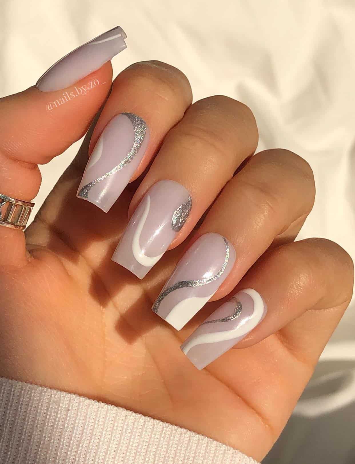A hand with medium milky white square nails accented with silver and white swirls