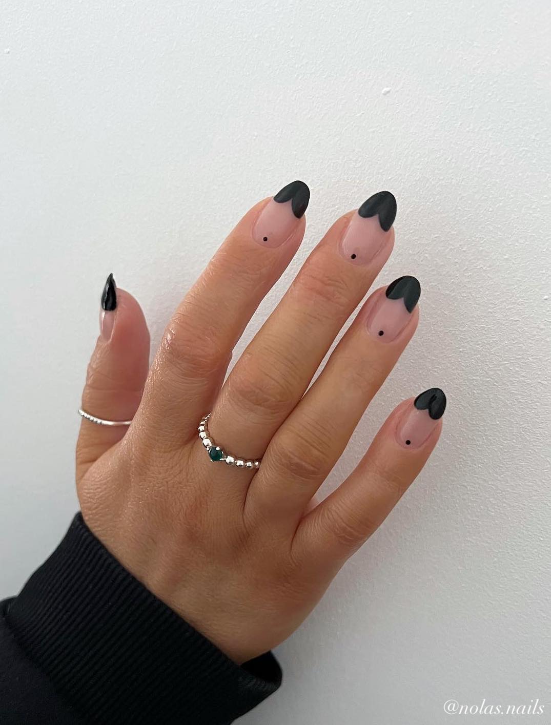 A hand with short nude almond nails featuring black scalloped French tips and a black dot detail