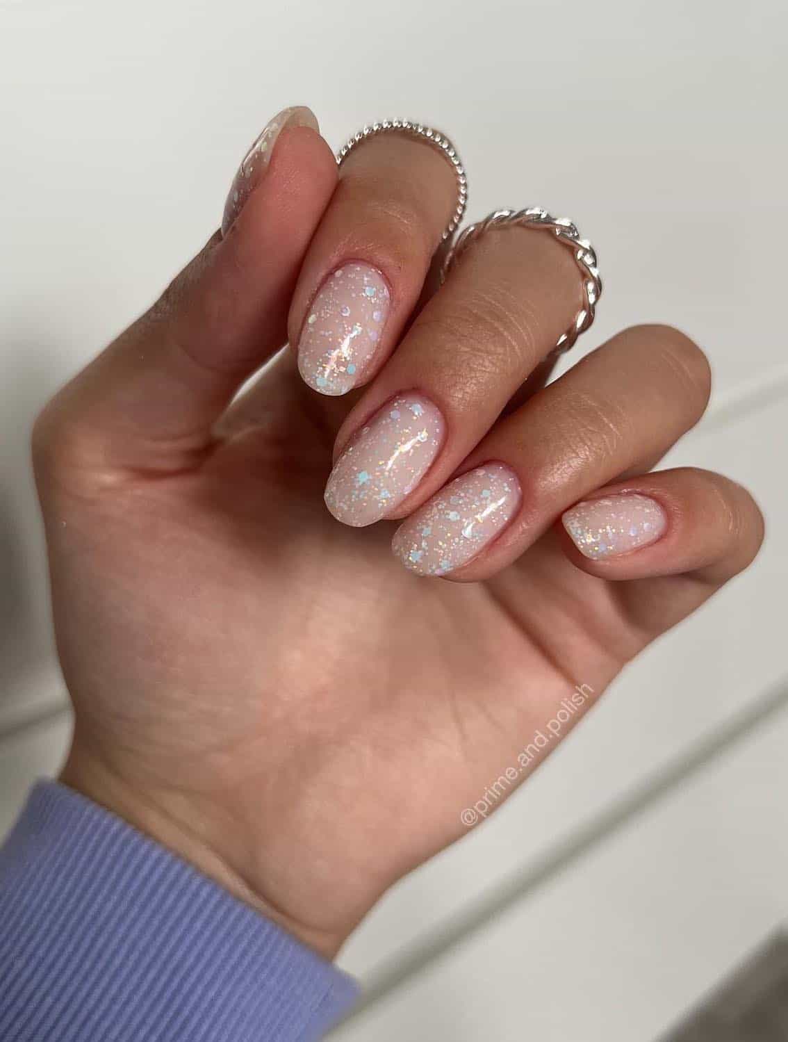 A hand with short round nails painted fully in a glitter nail polish