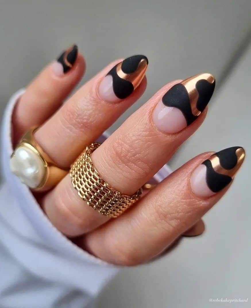 A hand with short almond nails painted with gold and black wavy French tips