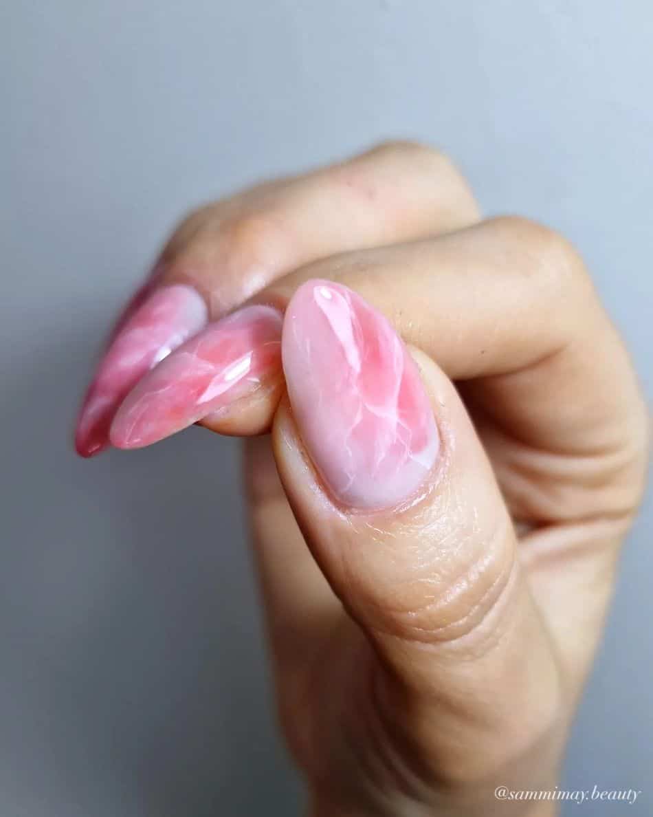 A hand with medium long almond nails painted with a white and pink marble design