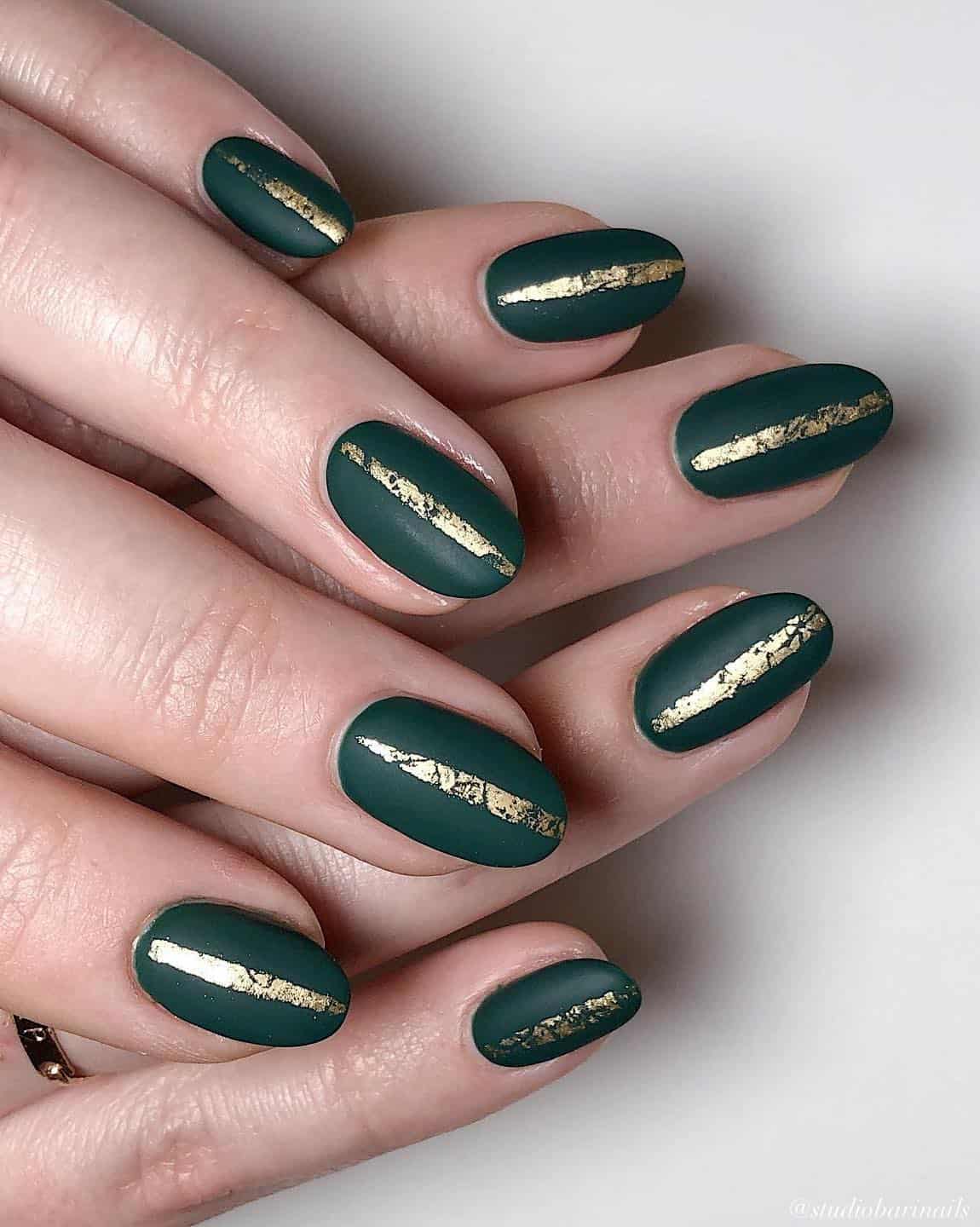 A hand with short round nails painted a matte forest green with vertical gold bands on each nail