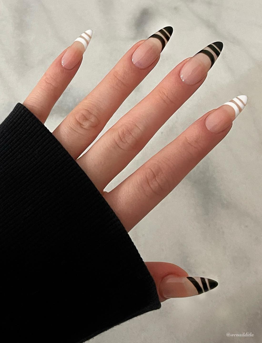 A hand with long nude almond nails painted in white and black French tips with negative space line details