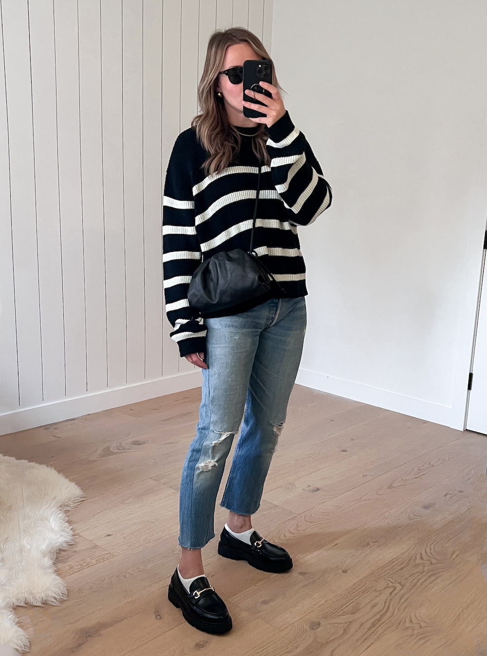 image of a woman wearing a striped black sweater with blue jeans and chunky black Gucci loafer dupes from H&M
