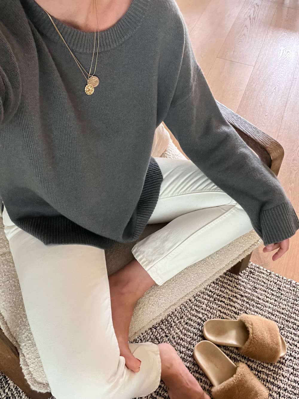 Up close image of a woman wearing a dark stormy blue cashmere sweater from Jenni Kayne, off-white jeans, and shearling slippers