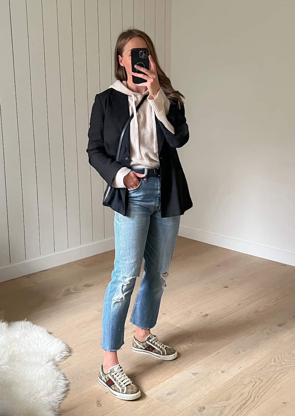 Christal wearing a black blazer over the Jenni kayne cashmere hoodie in oatmeal with blue jeans and beige sneakers