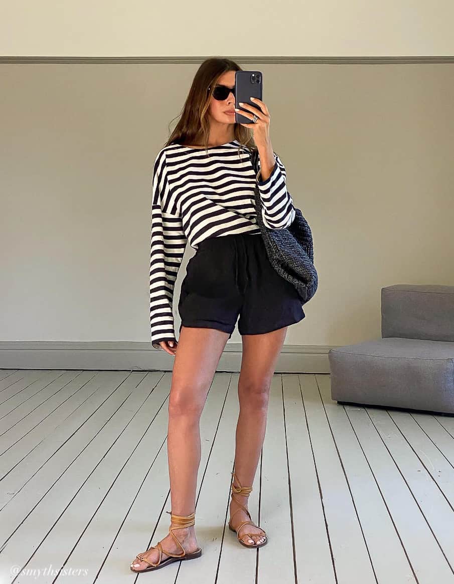 A woman wearing black linen shorts with a black and white striped long-sleeve top and tan gladiator sandals