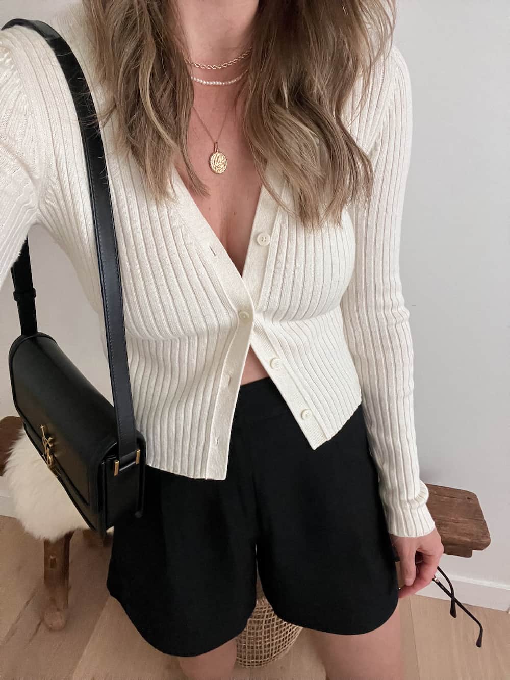 woman wearing a ribbed ivory cardigan with black linen shorts and a black shoulder bag
