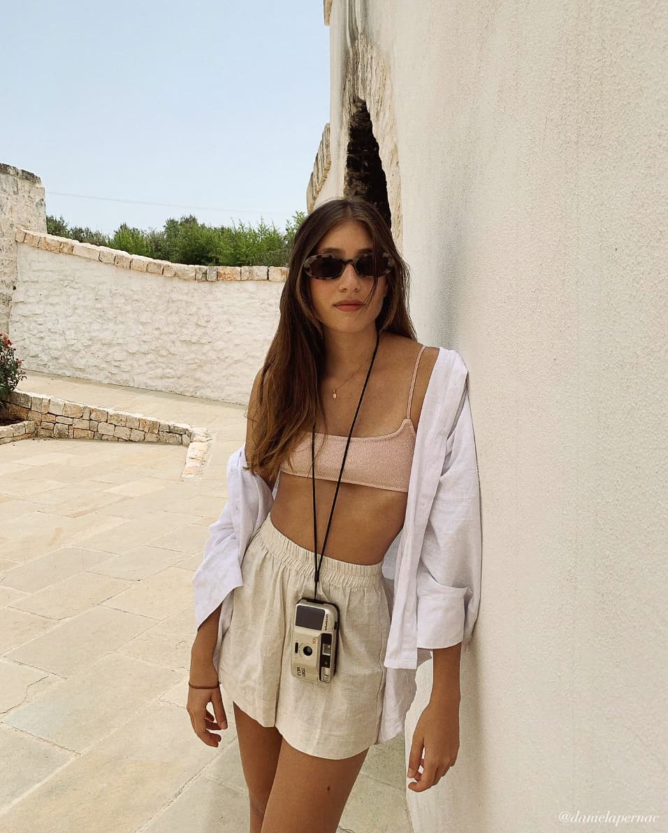 A woman wearing beige linen shorts with a tan bralette top and a white button-up