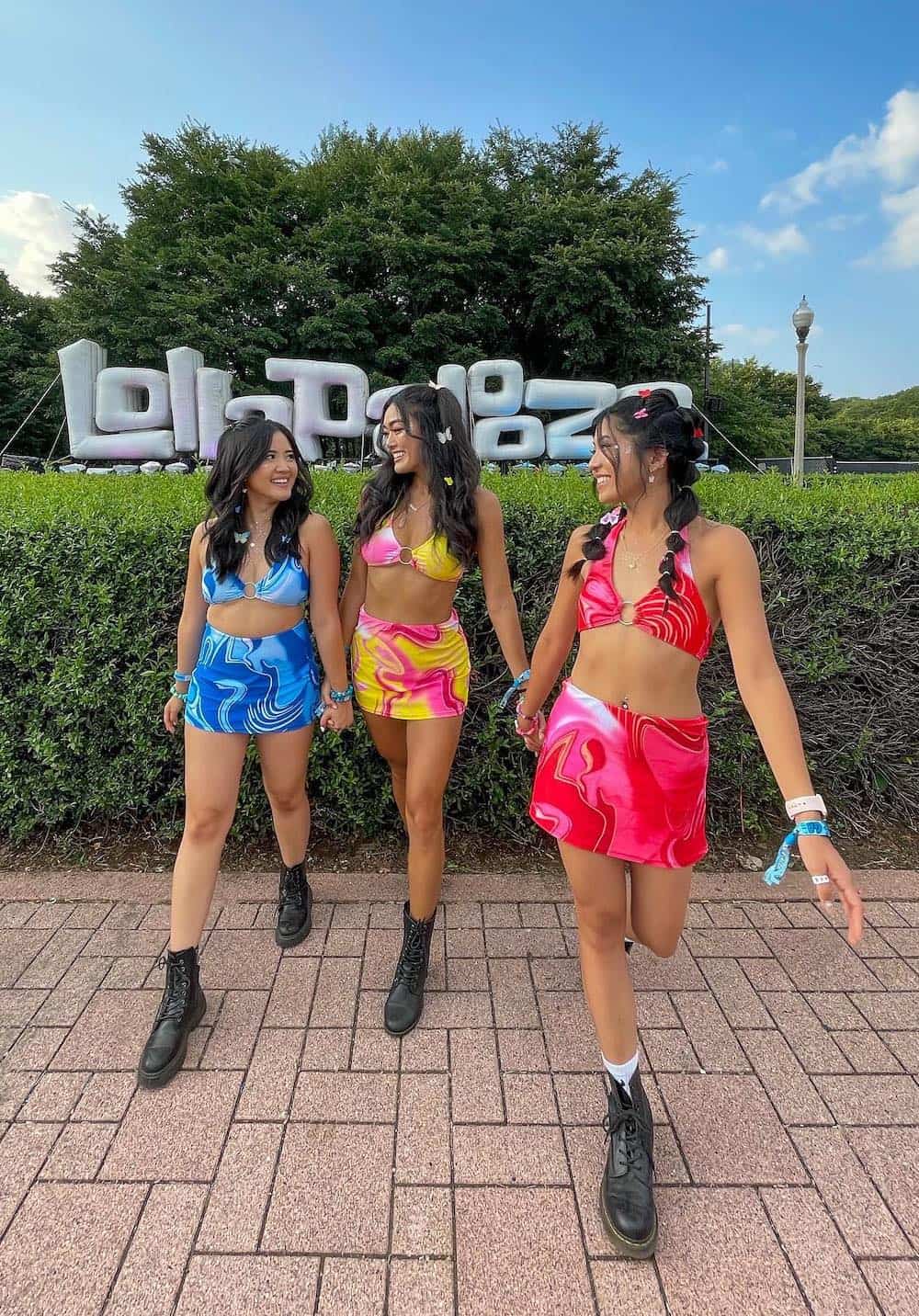 Three girls wearing matching red, blue, and yellow with pink tie-dye sets in front of a Lollapalooza sign